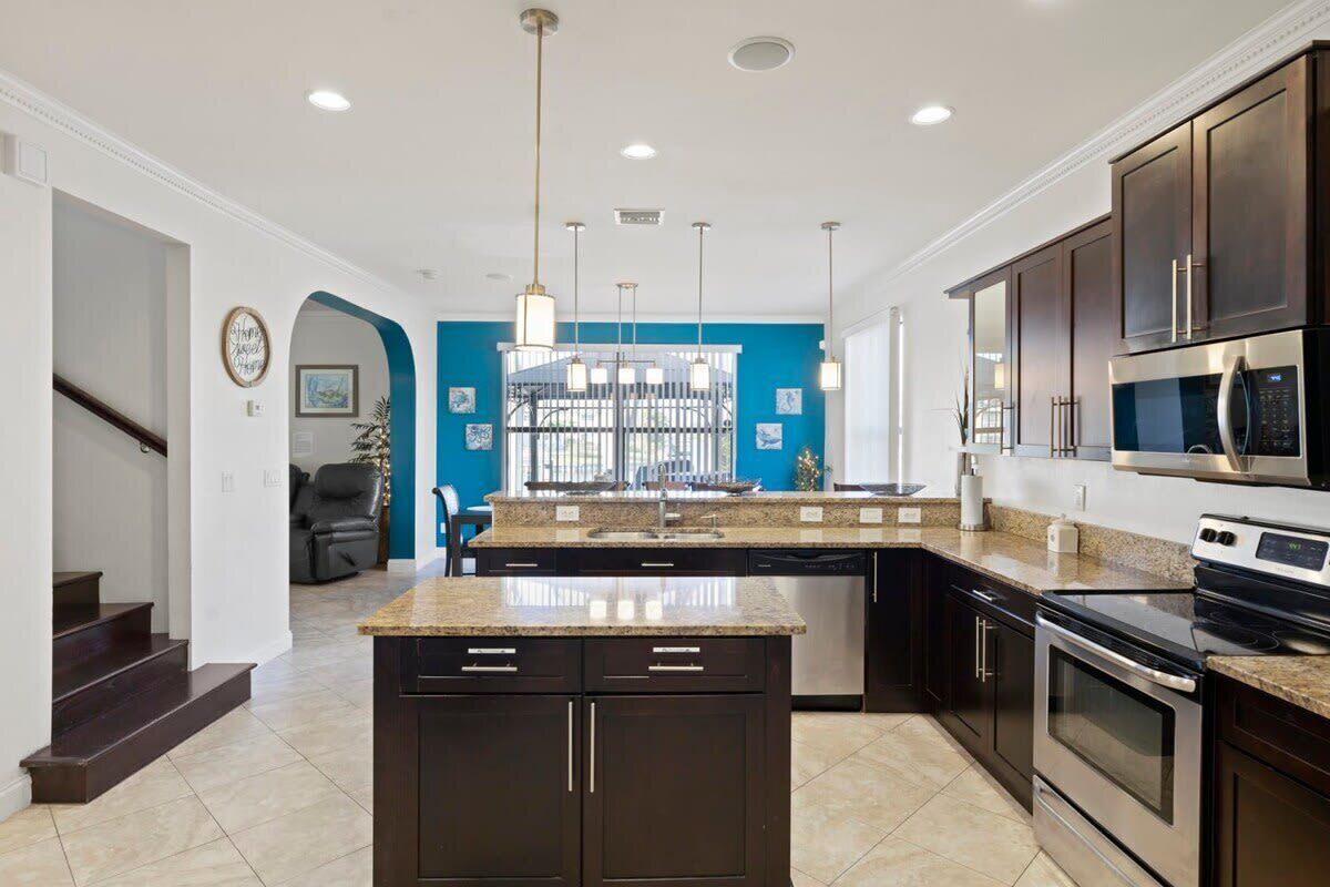 A modern kitchen with dark cabinetry, a central island, stainless steel appliances, and a blue accent wall.