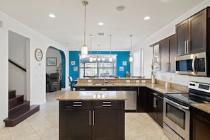 A modern kitchen with dark cabinetry, a central island, stainless steel appliances, and a blue accent wall. - Pristine Waterfront Villa in Cape Coral with Lagoon Style Pool Spa and Boat Lift (Cape Coral)