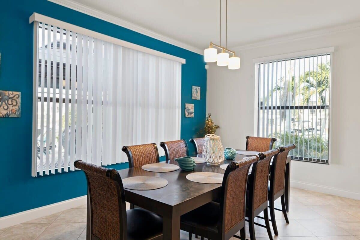 A dining area with a dark wooden table, wicker chairs, and white blinds.