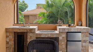 A compact kitchen with a stone countertop, a built-in sink, a refrigerator, and a wicker chair. - Pristine Waterfront Villa in Cape Coral with Lagoon Style Pool Spa and Boat Lift (Cape Coral)