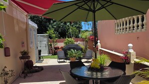 Un espace extérieur aménagé en terrasse, avec une table ronde et des chaises, un grand parasol et des plantes en pot.