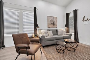A modern living room with a grey sofa, a brown leather chair, two small round tables, and a patterned rug.