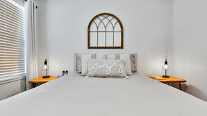A bedroom with a large bed, two bedside tables, a window with a wooden frame, and a wall-mounted clock. - The Silo Sweetheart- Just minutes from Downtown! (Waco)