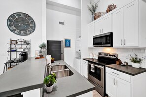 A modern kitchen with a central island, stainless steel appliances, white cabinetry, and a large wall clock.