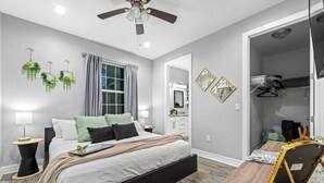 A modern bedroom with a bed, bedside tables, a ceiling fan, and a walk-in closet. - Pet-Friendly Home with a Hot Tub, Climbing Wall, King Bed & Gym by Mane Suites! (Tampa)