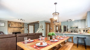 A dining area with a long wooden table set for four, a brown leather couch, and a kitchen in the background. - Private In the woods cabin With a Lakeview (Dawsonville)
