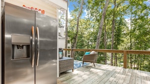 A stainless steel refrigerator on a wooden deck with a wicker chair and a small table, overlooking a forested area. - Private In the woods cabin With a Lakeview (Dawsonville)
