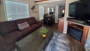 Ein Wohnzimmer mit braunem Sofa, einem Couchtisch, einem Fernseher und einer Treppe, die zu einer oberen Ebene führt.
