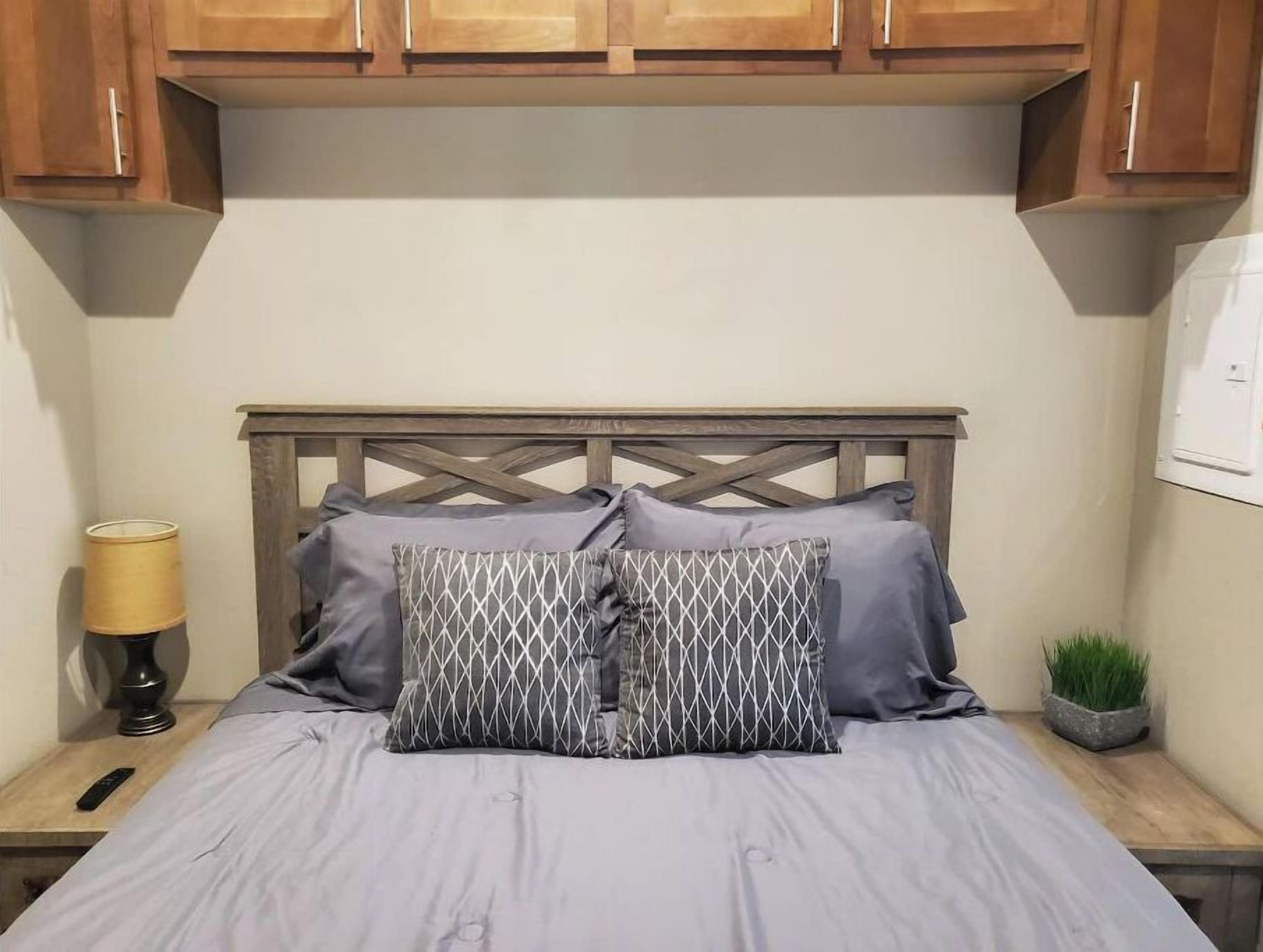 Un lit avec une tête de lit en bois, deux oreillers à motifs géométriques, une lampe de chevet et une petite plante en pot.