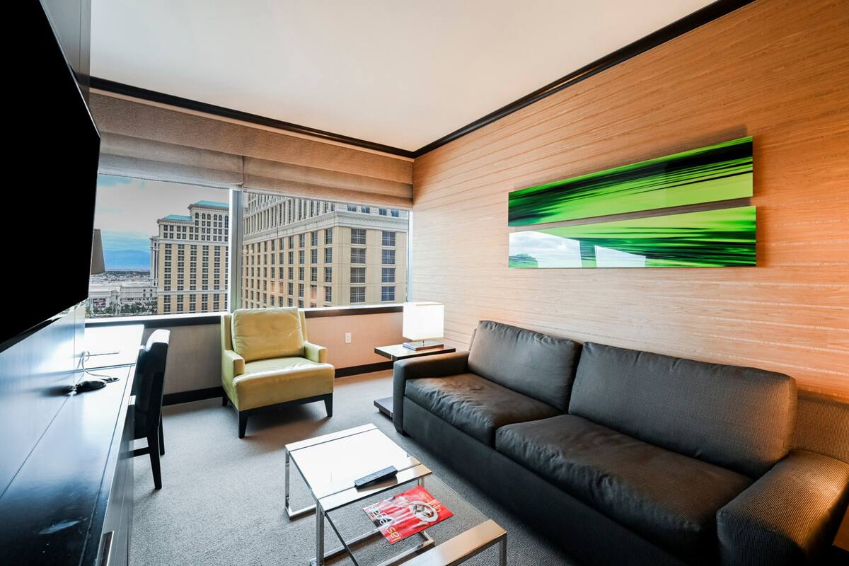 Ett modernt hotellrum med ett stort fönster, en soffa, en fåtölj, ett soffbord och en tv med platt skärm.