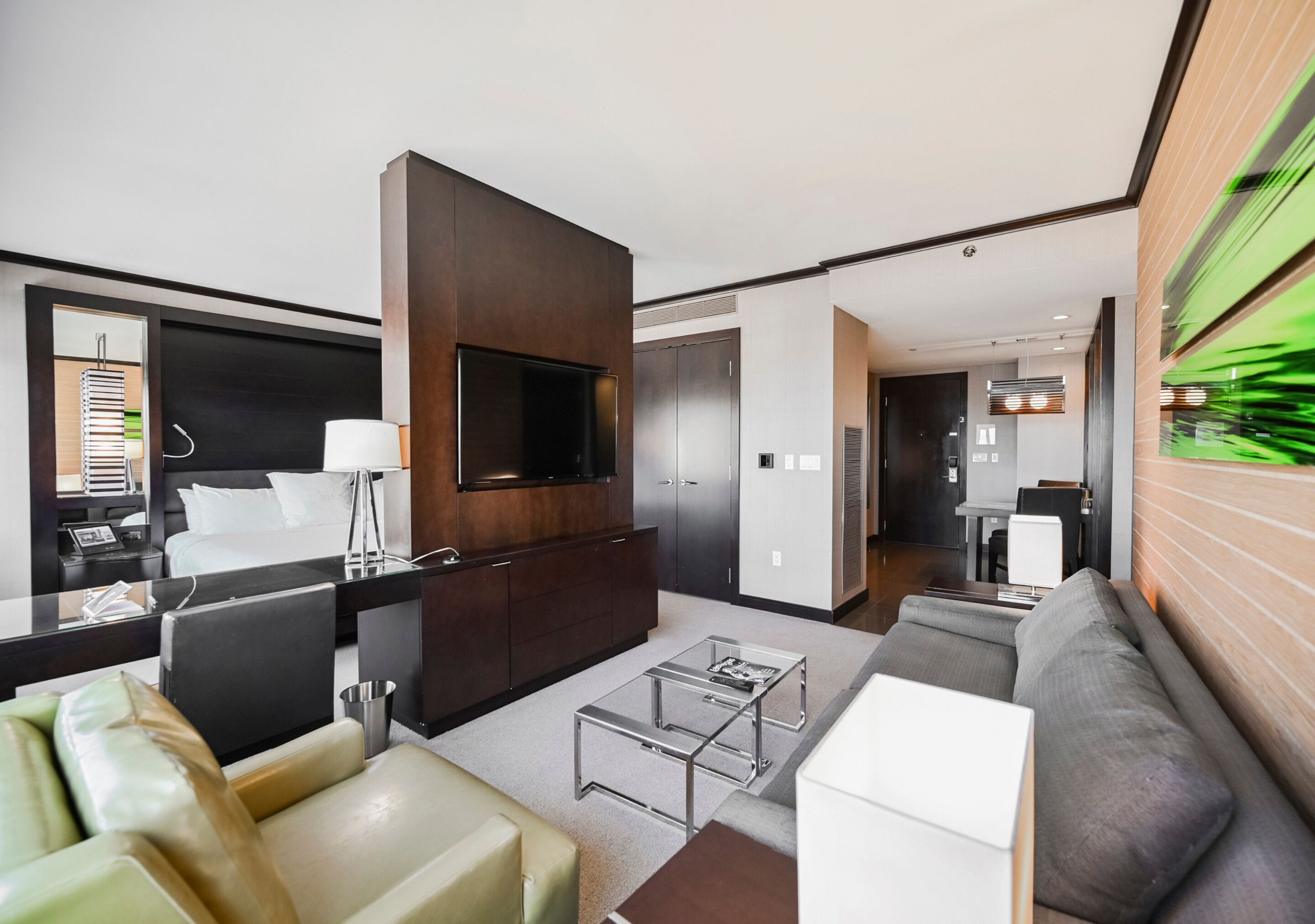 A modern hotel room with a large flat-screen TV, a sofa, a coffee table, and a dining area.