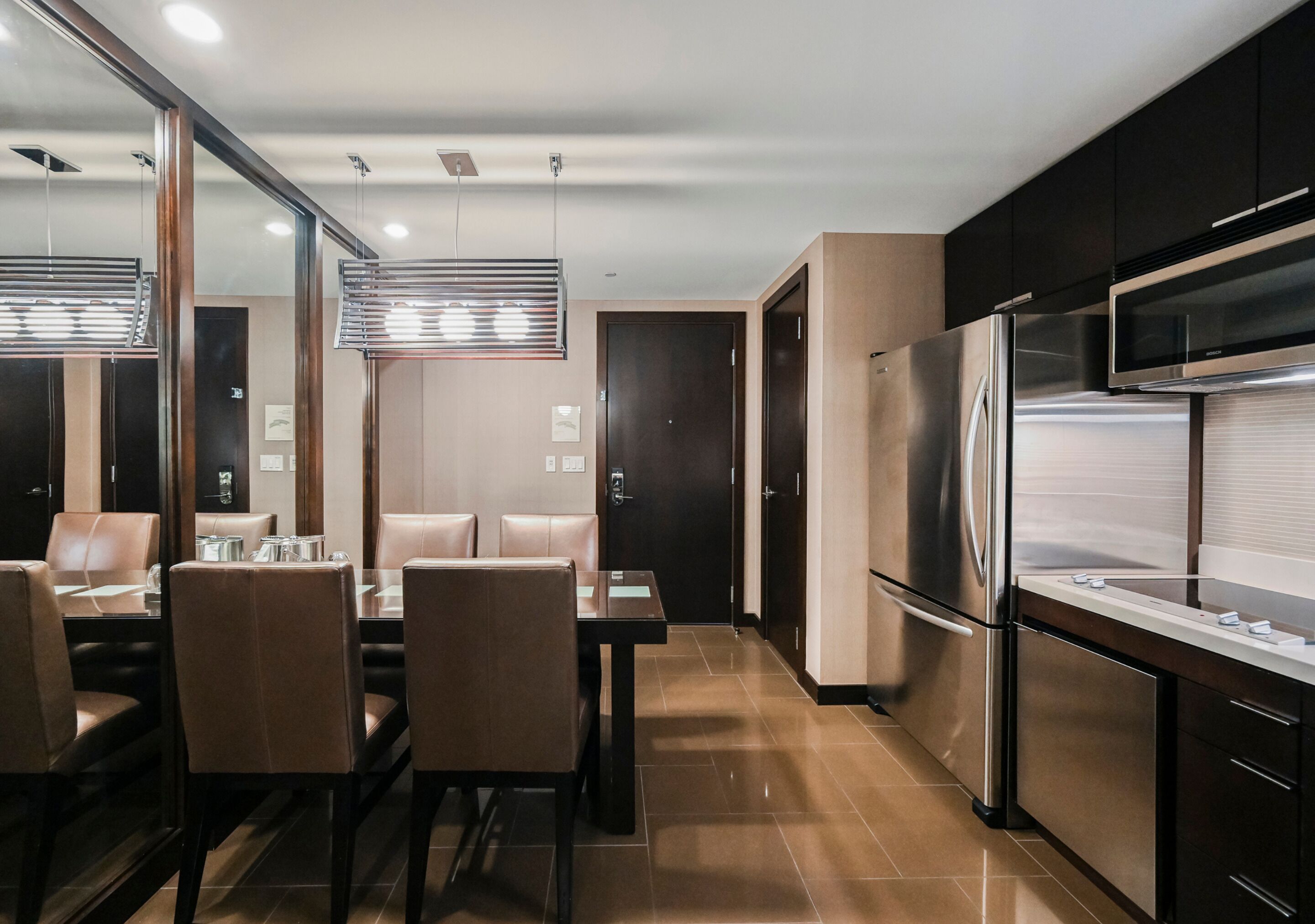 A modern kitchen with stainless steel appliances, a dining area with a table and chairs, and a large mirror reflecting the space.