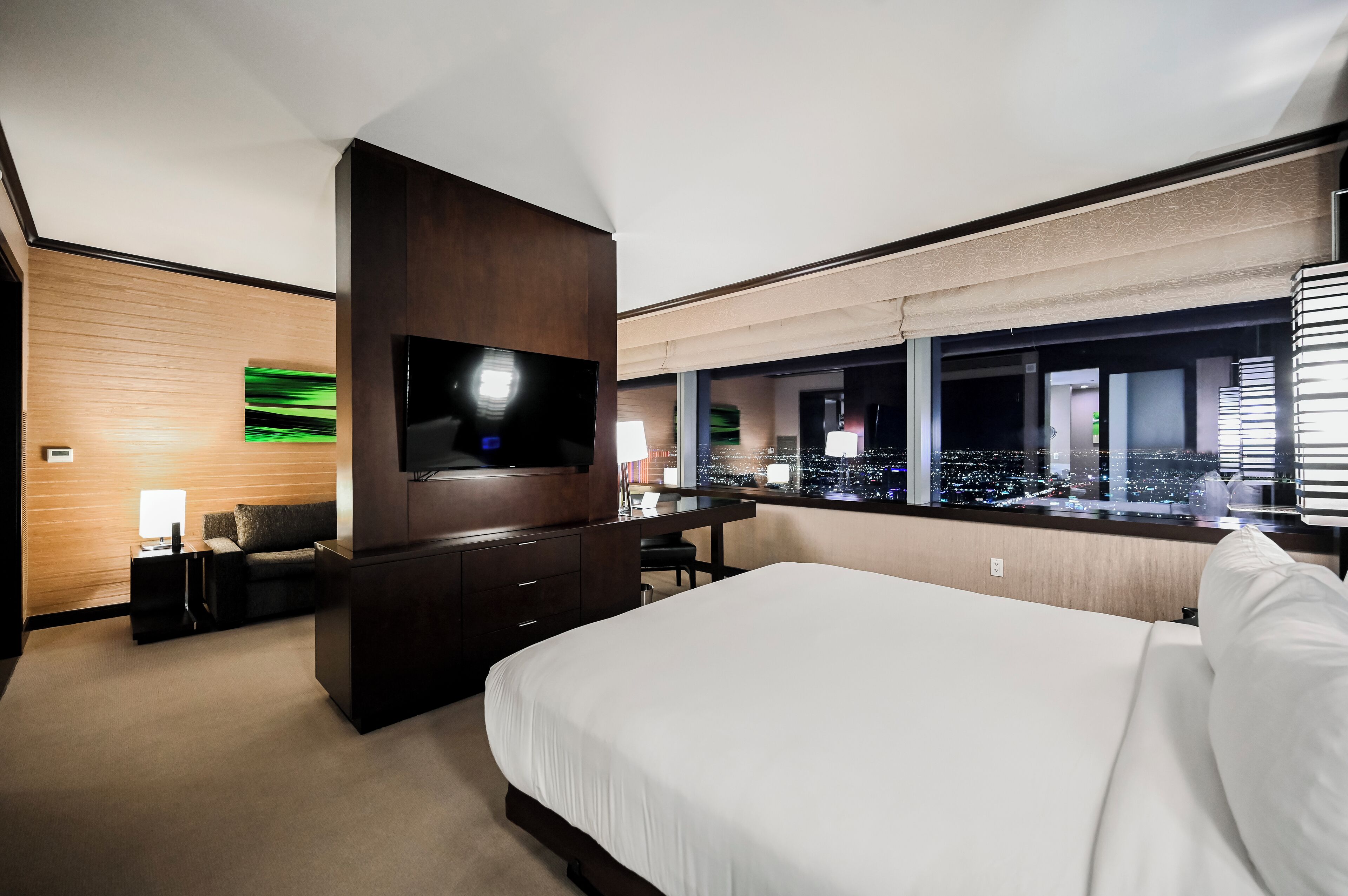A hotel room with a large bed, a TV, a desk, and a city view through the window.