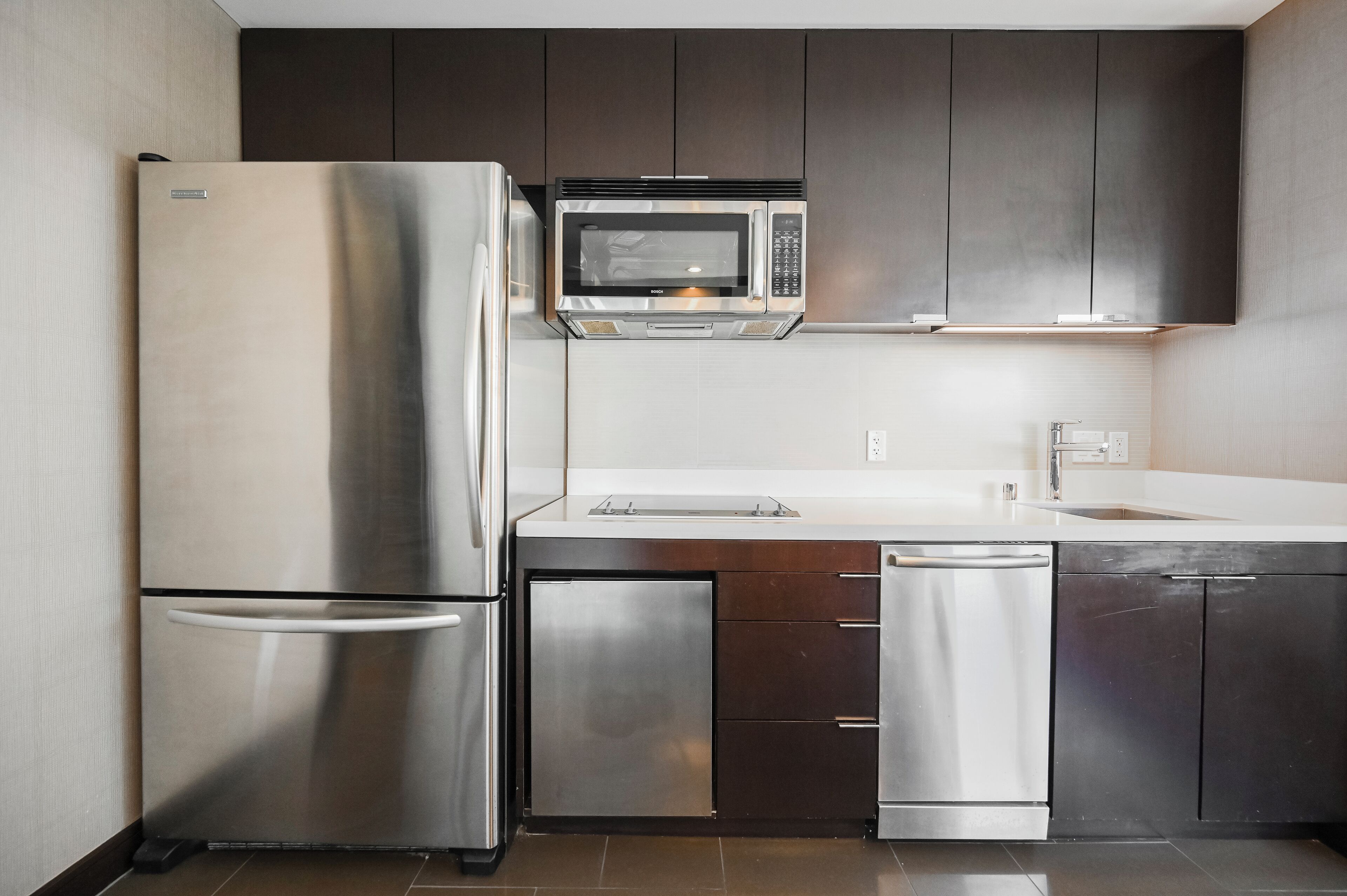 Una cocina moderna con electrodomésticos de acero inoxidable, incluyendo un refrigerador, microondas y lavavajillas, y gabinetes de madera oscura.