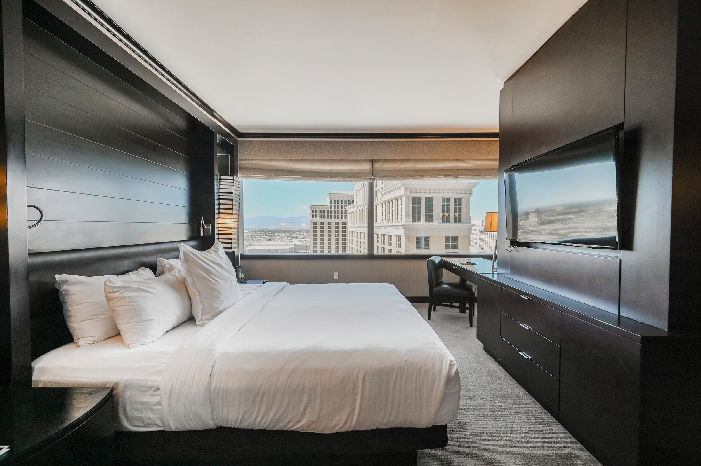 A modern hotel room with a large bed, a desk, and a TV.