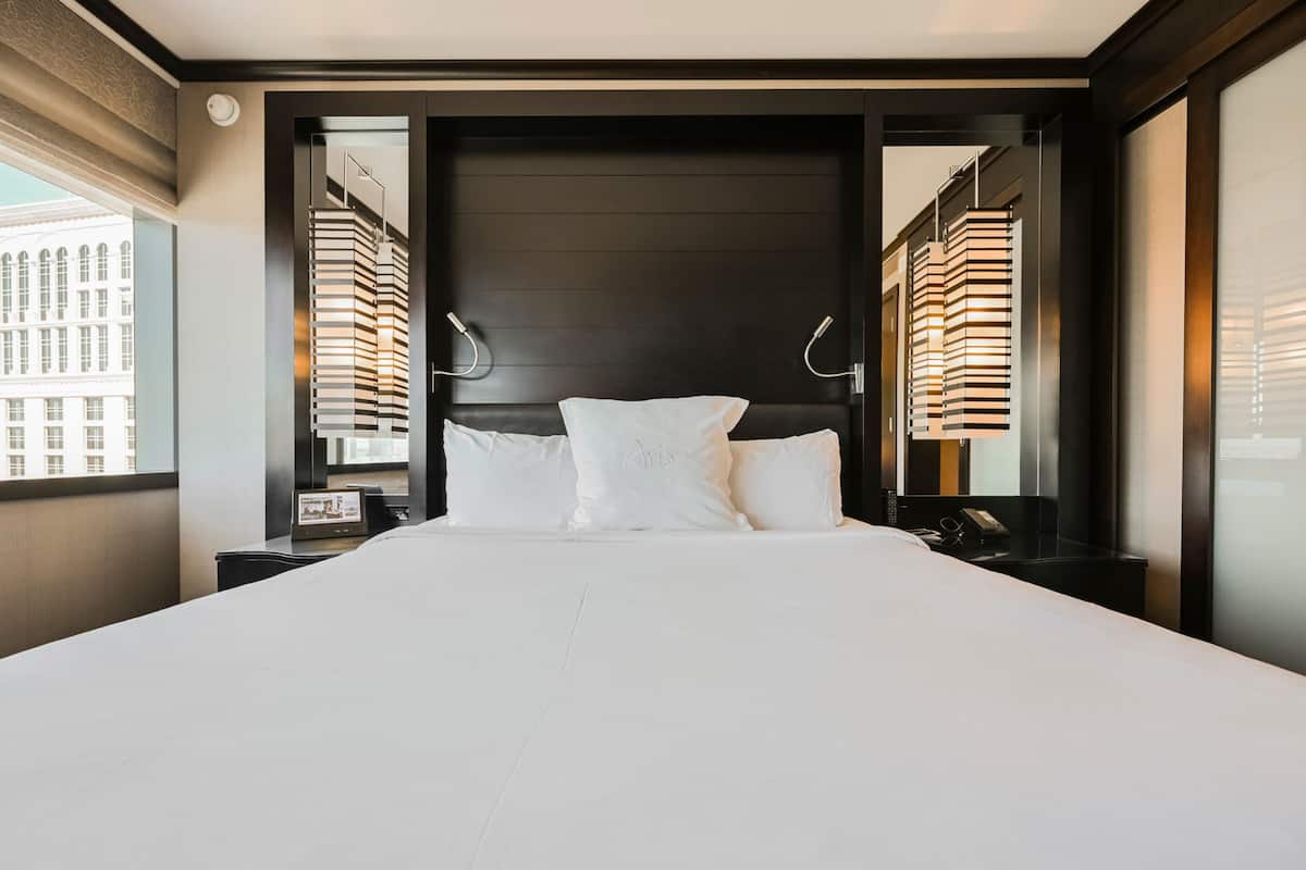 Ett modernt hotellrum med en stor säng, en mörk sänggavel och sänglampor.