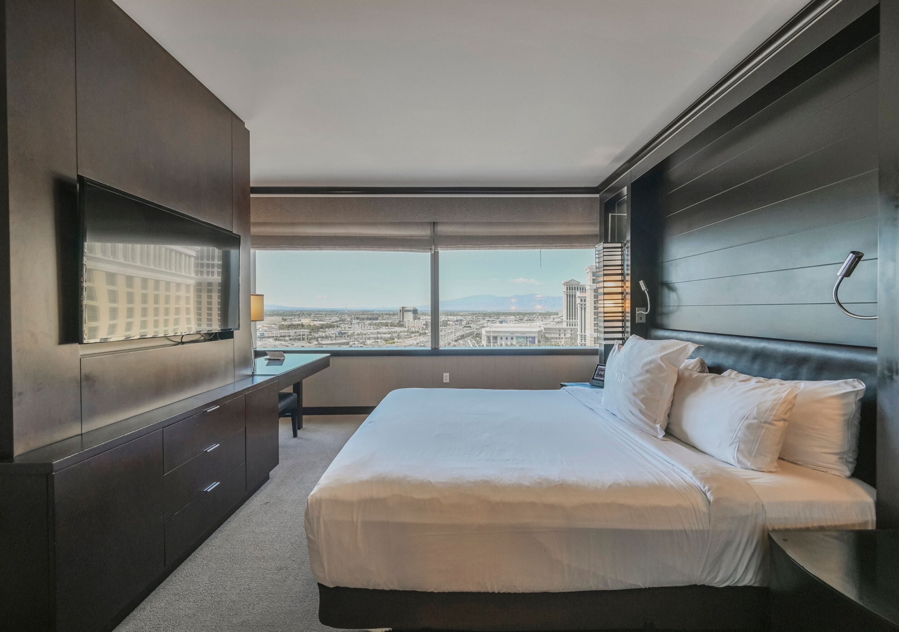 Ein modernes Hotelzimmer mit einem großen Bett, einem Schreibtisch und Blick auf die Stadtlandschaft.
