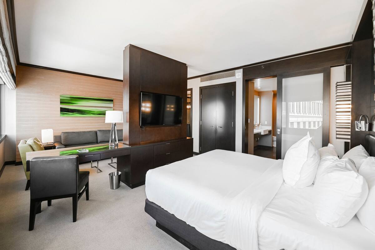 Ett modernt hotellrum med en stor säng, ett skrivbord, en TV och ett separat badrum.