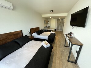 A hotel room with two beds, a desk, a TV, and a kitchenette.