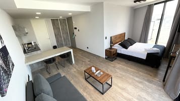 Una habitación de hotel moderna con cama, sofá, mesa de comedor y una pequeña cocina.
