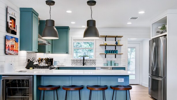Una cocina moderna con armarios color turquesa, un refrigerador de acero inoxidable y una barra con taburetes.