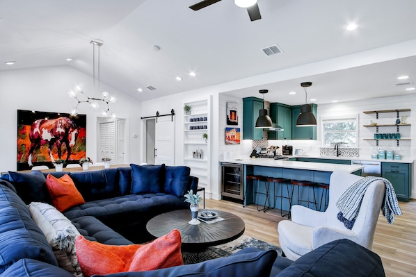 Een moderne woonkamer met een modulaire bank, een ronde salontafel en een keuken met turquoise kastjes en een barstoel.