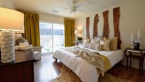 Ein Schlafzimmer mit Bett, Nachttisch, Lampe, Stuhl und Blick ins Freie.