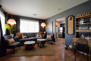 Una sala moderna con un sofá azul oscuro, mesas de centro redondas y una barra para cócteles con copas.