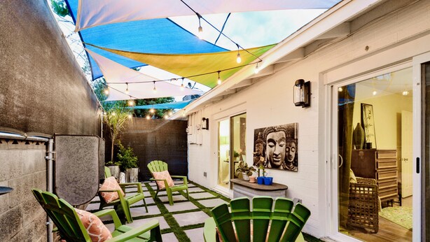 Eine Terrasse mit grünen Stühlen und einem Tisch, einem großen Sonnenschirm und Blick ins Haus.