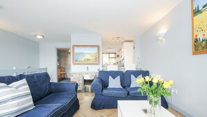 A living room with a sofa, a dining table, and a kitchen in the background. - Slipway 16 (Wadebridge)
