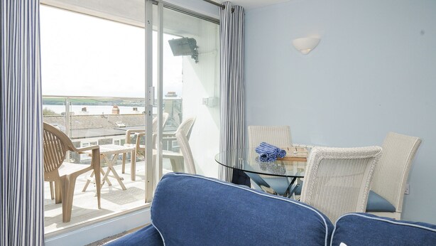 A room with a glass door leading to a balcony, a table with chairs, and a view of the sea. - Slipway 16 (Wadebridge)