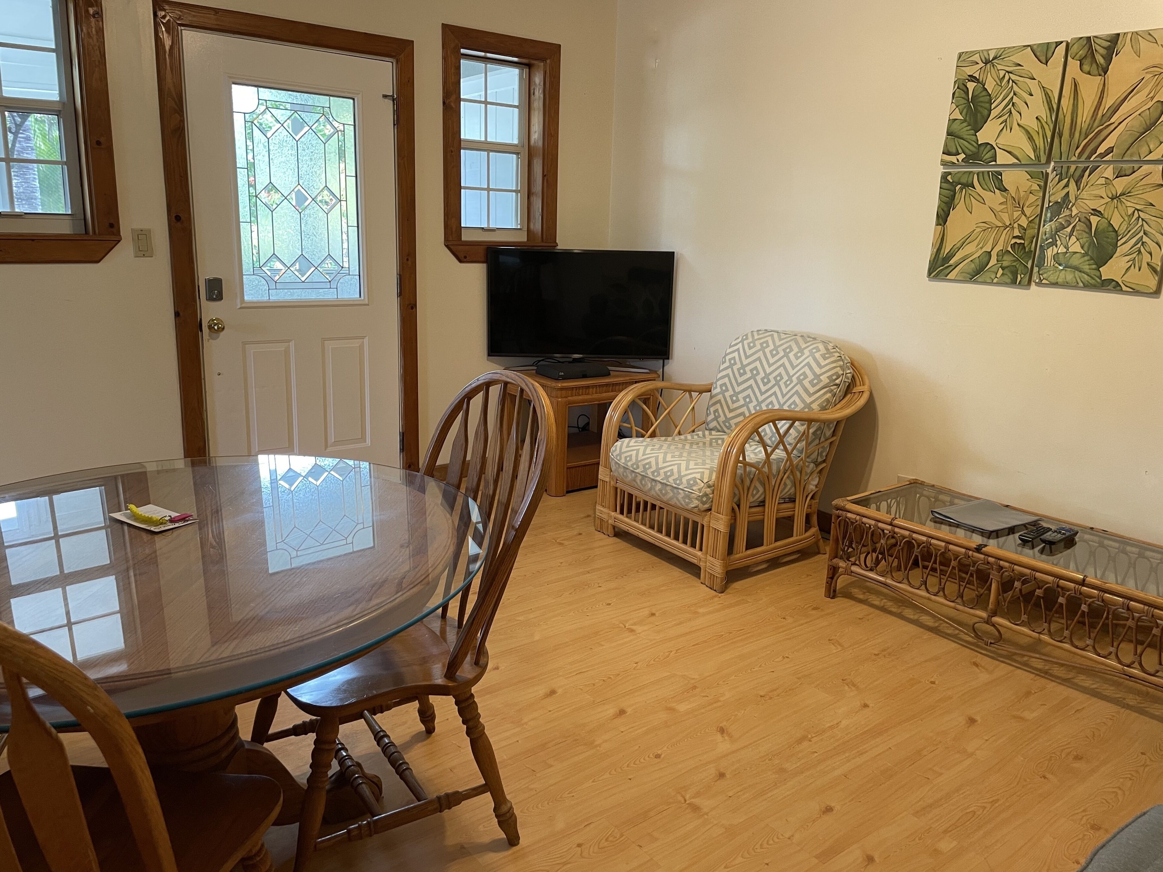 A living room with a glass-top dining table, wicker chairs, a television, and a small side table.