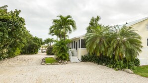 Een huis met een grindpad, palmbomen en een klein vijvertje.