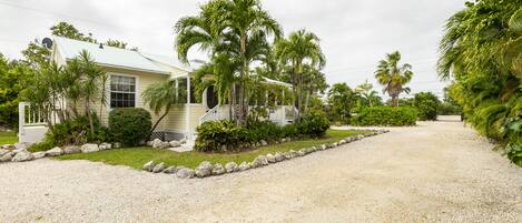 A house with a gravel driveway, surrounded by palm trees and a well-maintained lawn.