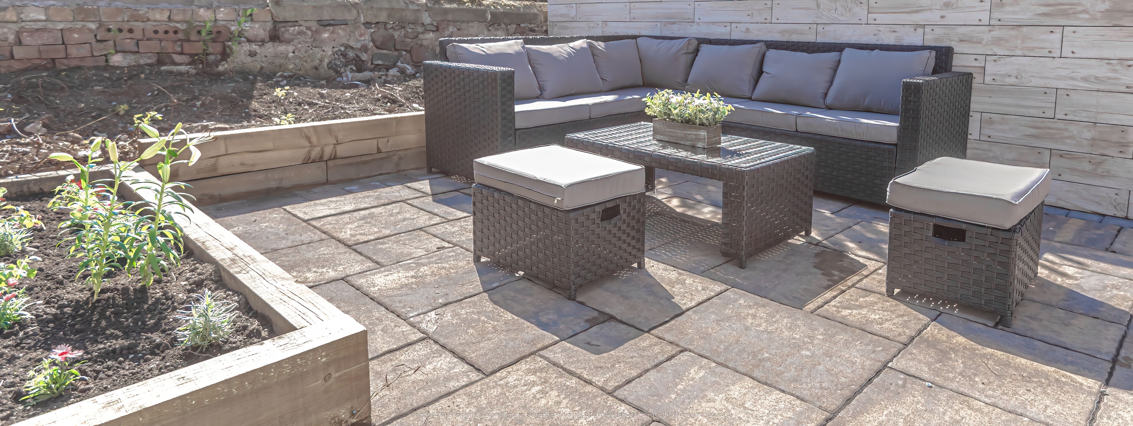 An outdoor patio with wicker furniture, including a sofa and two square tables.