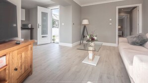 A modern living room with a wooden cabinet, a glass coffee table, and a white sofa. - Lovely 1-bed Cottage in Kelty With Hot Tub (Kelty)
