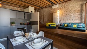 A modern kitchen with grey cabinets, a dining table set with plates and glasses, and a brick wall with a sofa and cushions. - VELLUTO Luxury open space mezzanine and terrace self check in (Venezia)