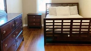 A bedroom with a wooden bed, a dresser, a nightstand, and a ceiling fan. - Downstairs Getaway By the Beach (Galveston)