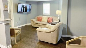 A living room with a beige sofa, a small table, and a TV mounted on the wall. - Downstairs Getaway By the Beach (Galveston)