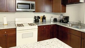 A kitchen with wooden cabinets, a stainless steel microwave, a stove, and a sink. - Downstairs Getaway By the Beach (Galveston)