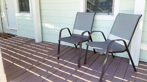 A covered porch with two chairs and a window. - Downstairs Getaway By the Beach (Galveston)