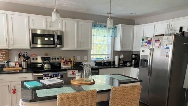 A modern kitchen with white cabinets, stainless steel appliances, a central island with chairs, and a refrigerator with magnets. - Escape to the Cape in this brand new, family-friendly, centrally located home. (South Dennis)