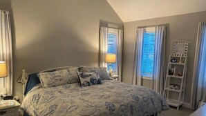 A bedroom with a bed, nightstands, a bedside table, a lamp, a window with blinds, a shelf, and a ladder. - Escape to the Cape in this brand new, family-friendly, centrally located home. (South Dennis)