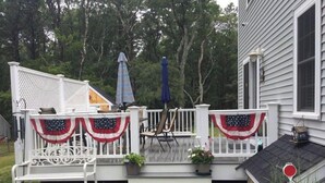 A deck with white railings, a bench, and American flags. - Escape to the Cape in this brand new, family-friendly, centrally located home. (South Dennis)