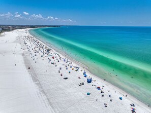 A beach with a long stretch of white sand, clear turquoise water, and a few umbrellas.