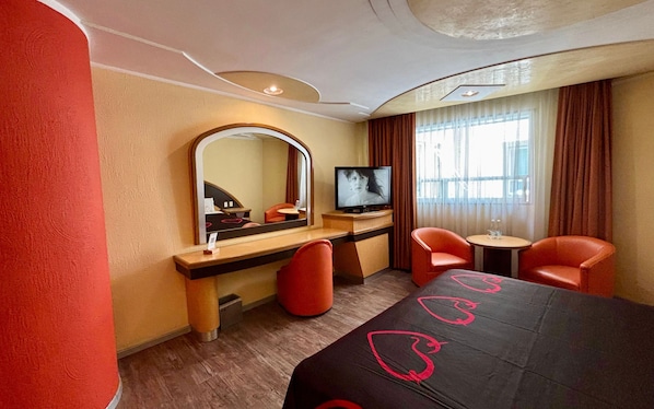 A hotel room with a bed, a TV, a desk, two chairs, and a mirror.
