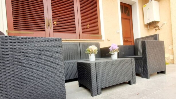 Un patio con mobiliario de mimbre, incluyendo un sofá y una mesita de centro, y una pequeña planta en maceta.