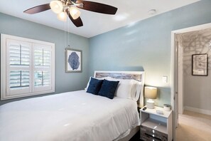 Un dormitorio con cama, mesita de noche, ventilador de techo y ventana con persianas.