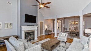 A spacious living room with a fireplace, a television, and a dining area with a chandelier. - Luxury in Rumbling Bald Resort ~ WiFi ~ Community Beach, Pool, Golf and more (Lake Lure)