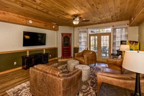 A living room with wooden ceiling, a television, leather sofas, a fireplace, and a large window.